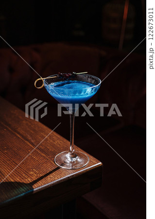 Elegant blue cocktail served in a classic glass on a wooden table in an intimate bar setting at night 122673011