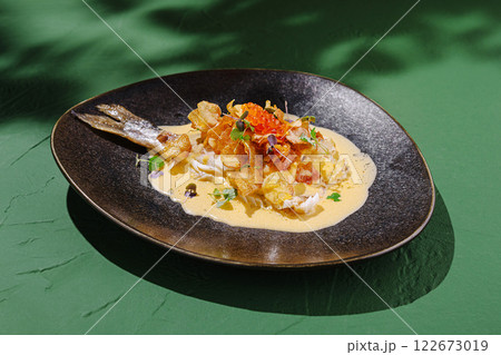 Gourmet dish featuring fried fish on a bed of creamy sauce with crispy toppings, set on a vibrant green surface Gourmet dish featuring fried fish on a bed of creamy sauce with crispy toppings, set on a vibrant green surface 122673019