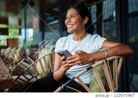 Smiling Woman Engaging with Smartphone in Modern Caf Setting 122675967