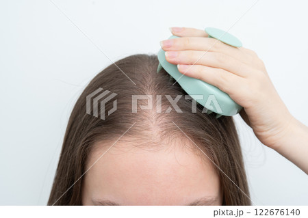 Woman using a scalp massager to stimulate hair growth and care for scalp with copy space. Concept of beauty treatment, wellness, and addressing alopecia and thinning hair through daily routines. Woman using a scalp massager to stimulate hair growth and care for scalp with copy space. Concept of beauty treatment, wellness, and addressing alopecia and thinning hair through daily routines. 122676140