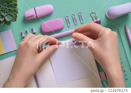 Blank notepad page for your text in pastel colored stationery frame. A woman attaches a note with a paperclip. Background in mint green color. 122676173