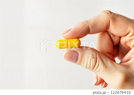 Hand holding yellow capsule pill. 122676418