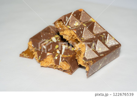 Trend Dubai chocolate bar with peanut butter, sticky caramel and kataifi dough filling on white background. Confectionery and sweets. Trend Dubai chocolate bar with peanut butter, sticky caramel and kataifi dough filling on white background. Confectionery and sweets. 122676539