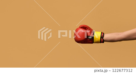 Arm extended wearing red boxing glove, fist clenched in straight jab against warm brown background, symbolizing strength and discipline. 122677312