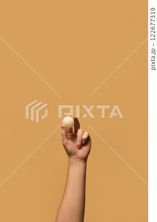 Hand holding small white ping pong ball between fingers, highlighting focus and control in precision-based table tennis matches against beige background. Hand holding small white ping pong ball between fingers, highlighting focus and control in precision-based table tennis matches against beige background. 122677319