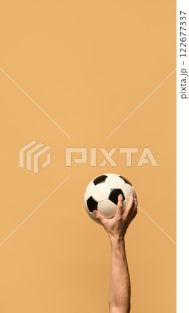 Hand gripping soccer ball high, fingers pressing against black-and-white panels, representing strength, control, and energy essential for competitive play. Hand gripping soccer ball high, fingers pressing against black-and-white panels, representing strength, control, and energy essential for competitive play. 122677337