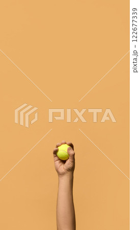 Hand gripping tennis ball firmly, showcasing control, readiness, and confidence before serve or rally against warm-toned background. 122677339
