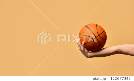 Arm extended outward, gripping basketball firmly, demonstrating stability, technique, and readiness to make powerful play against warm-toned background. Arm extended outward, gripping basketball firmly, demonstrating stability, technique, and readiness to make powerful play against warm-toned background. 122677345