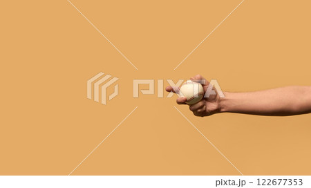 Hand gripping baseball firmly from below, illustrating control, concentration, and athletic preparation against warm-toned background. 122677353