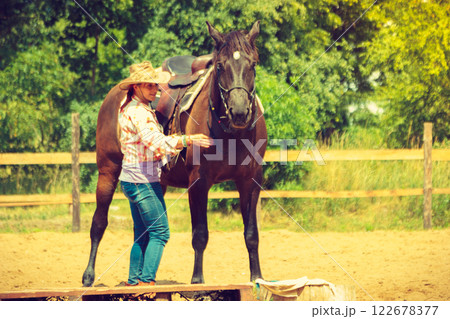 Cowgirl getting horse ready for ride on countryside 122678377