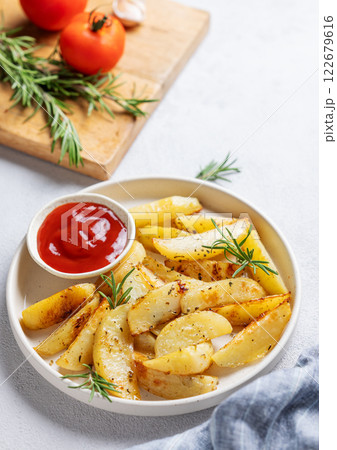 Baked potato wedges with spices, fresh rosemary and tomato sauce on a wooden board  122679616