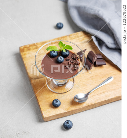 Chocolate pudding in a glass with fresh blueberries and mint on a wooden board on a light background 122679622