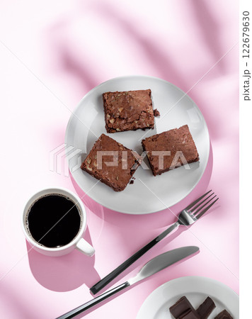 Pieces of chocolate brownie with nuts on a plate with a cup of espresso coffee on a pink background 122679630