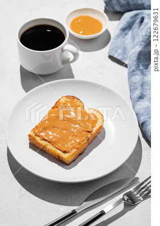 Peanut butter toast on a plate on a light background with a cup of freshly brewed coffee and napkin. 122679631