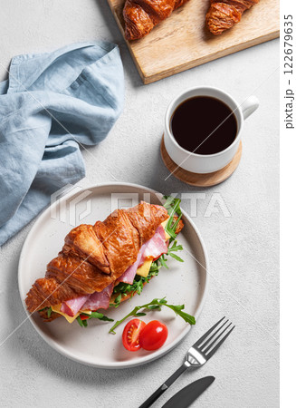 Croissant sandwich with ham, cheese, tomato and arugula on a plate on a light background Croissant sandwich with ham, cheese, tomato and arugula on a plate on a light background 122679635