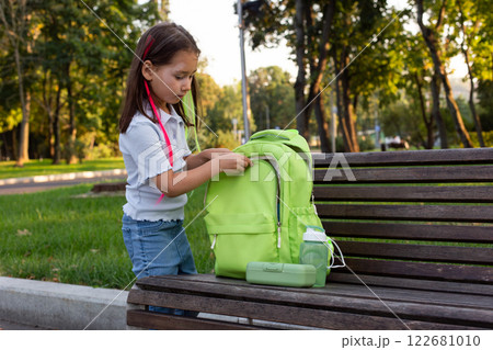 Young girl with green backpack in park getting ready for school 122681010