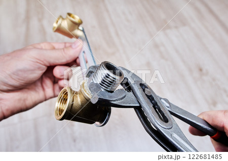 Water pump pliers are used to tighten a stainless steel threaded nipple wrapped in plumbing flax into brass fitting for secure installation. Water pump pliers are used to tighten a stainless steel threaded nipple wrapped in plumbing flax into brass fitting for secure installation. 122681485