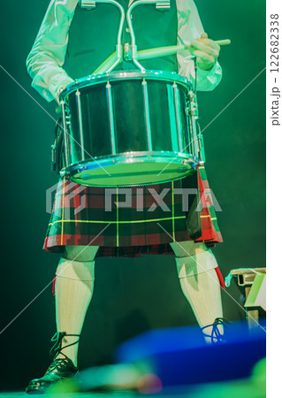 Holiday of St. Patrick's Day, music. Scottish drummer with traditional kilt performing live on stage close-up. Drumsticks in hand, vibrant stage 122682338