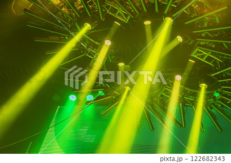 Dynamic yellow stage lights shining from a circular structure with green glowing background. Concept of vibrant concert lighting, festive atmosphere Dynamic yellow stage lights shining from a circular structure with green glowing background. Concept of vibrant concert lighting, festive atmosphere 122682343