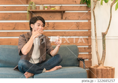 家のリビングでスマホを見ながらくつろぐ若いアジア人男性(驚く・ショック・衝撃・ビックリ) 家のリビングでスマホを見ながらくつろぐ若いアジア人男性(驚く・ショック・衝撃・ビックリ) 122685257