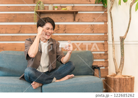 家でくつろぎながらスマホ・スマートフォンでスポーツ観戦する若いアジア人男性（ガッツポーズ・嬉しい） 122685262