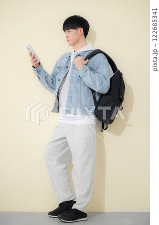 リュックを背負ってスマホを持つ男の子の全身　春ぽい黄色背景 122685341