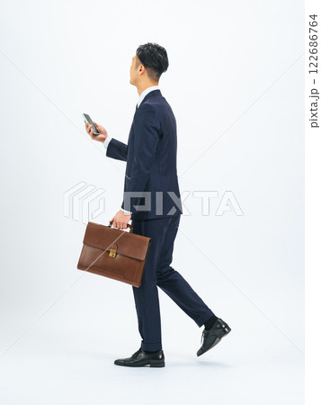 スマホを持って歩くミドルエイジ男性ビジネスパーソンの後ろ姿の全身写真 スマホを持って歩くミドルエイジ男性ビジネスパーソンの後ろ姿の全身写真 122686764