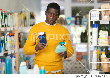 Before buying in household shop, African male customer choose glass cleaner spray 122687413
