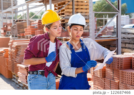 Two female storekeepers are discussing work issues in the warehouse, holding an estimate in their hands 122687466