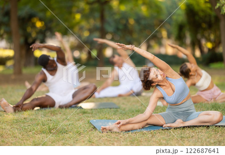 Woman doing Parivrtta Janu Sirsasana during group yoga outdoors 122687641