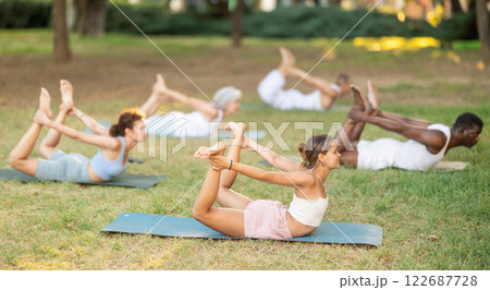 Girl performing Bow Pose during group yoga class in park Girl performing Bow Pose during group yoga class in park 122687728