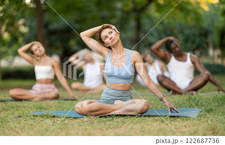 Multinational yoga enthusiasts with female coach perform padmasana in park 122687736