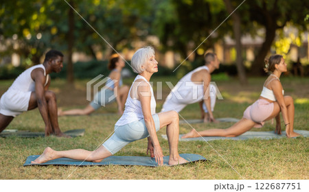 Senior woman performing Anjaneyasana at group yoga session outdoors 122687751