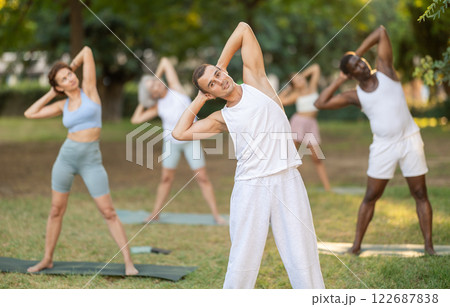 Man performing Bending Tree Pose during group yoga in park 122687838