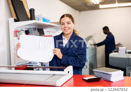 Happy young woman in uniform checking the print quality and accepting color proofs in the printer house Happy young woman in uniform checking the print quality and accepting color proofs in the printer house 122687932