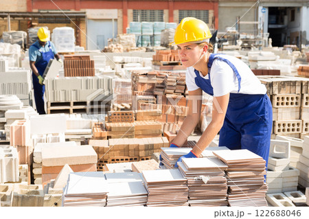 Young attentive female worker lays tiles in a warehouse Young attentive female worker lays tiles in a warehouse 122688046