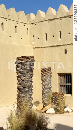 Arabic fort courtyard highlights tall palm trunks and natural desert landscaping. Courtyard design emphasizes fort walls with small openings, blending desert functionality with cultural heritage. 122690887