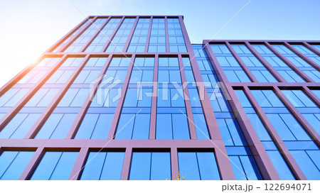 Glass building with transparent facade of the building and blue sky. Structural glass wall reflecting blue sky. Abstract modern architecture fragment. Contemporary architectural background. 122694071