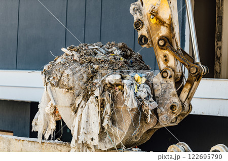A construction excavator bucket filled with dirt, debris, and trash, showcasing urban waste management and construction site cleanup activities A construction excavator bucket filled with dirt, debris, and trash, showcasing urban waste management and construction site cleanup activities 122695790