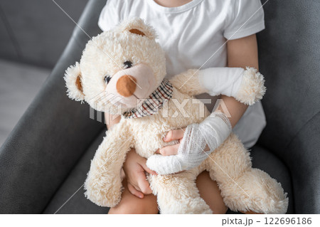 Little girl with broken finger holds teddy bear with a bandaged paw at the doctor's appointment in the hospital 122696186