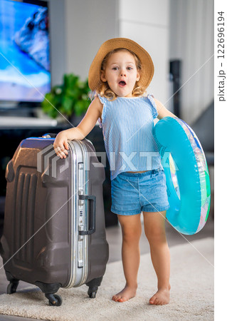 Little girl with suitcase baggage luggage and inflatable life buoy ready to go for traveling on vacation Little girl with suitcase baggage luggage and inflatable life buoy ready to go for traveling on vacation 122696194