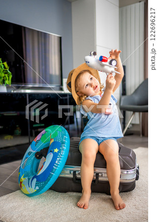 Little girl with suitcase baggage luggage and inflatable life buoy playing with toy plane and ready to go for traveling on vacation 122696217