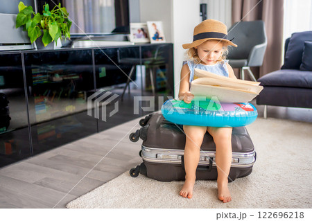 Little girl with suitcase baggage luggage and inflatable life buoy reading map and ready to go for traveling on vacation 122696218