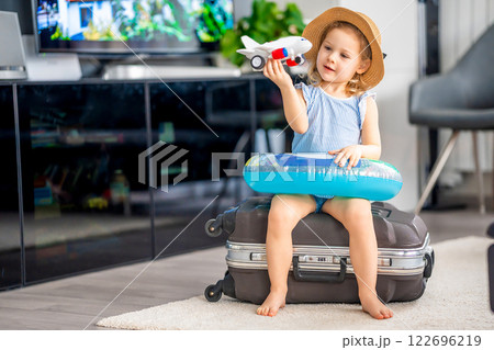 Little girl with suitcase baggage luggage and inflatable life buoy playing with toy plane and ready to go for traveling on vacation 122696219