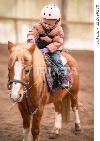 Little Child Riding Lesson. Three-year-old girl rides a pony and does exercises 122696270