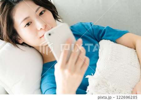 寝転んでスマホを見る若い女性 122696285