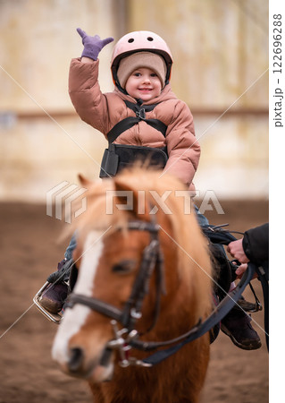 Little Child Riding Lesson. Three-year-old girl rides a pony and does exercises Little Child Riding Lesson. Three-year-old girl rides a pony and does exercises 122696288