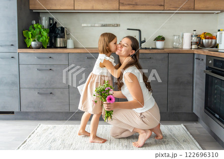 Little girl giving bouquet of flowers and drawing to her mum on the home kitchen. Mothers day, birthday or International Women's Day 8 march concept Little girl giving bouquet of flowers and drawing to her mum on the home kitchen. Mothers day, birthday or International Women's Day 8 march concept 122696310