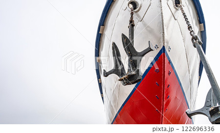 Ship's bow with a red and white hull, flanked by two large anchors on chains close-up. Vessel is docked on dry land for maintenance 122696336