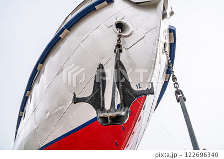 Ship's bow with a red and white hull, flanked by two large anchors on chains close-up. Vessel is docked on dry land for maintenance Ship's bow with a red and white hull, flanked by two large anchors on chains close-up. Vessel is docked on dry land for maintenance 122696340